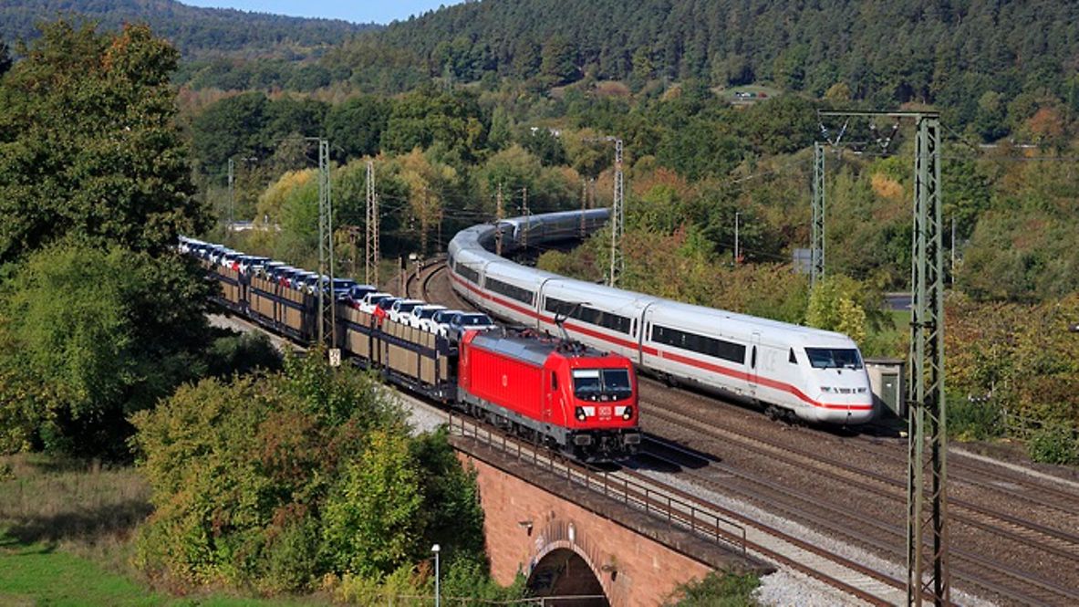 Ein Güterzug und eine ICE fahren nebeneinander über eine Brücke.